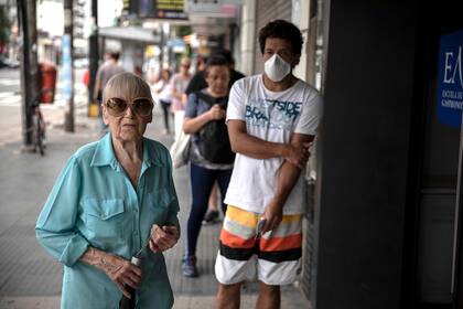 Hilda Málaga, de 83 años, espera para cobrar la jubilación acompañada por Mariana, su ahijada