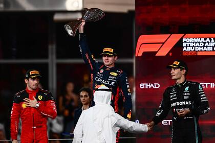 Red Bull Racing's Dutch driver Max Verstappen (C) raises the winners' trophy as he stands on the podium with Ferrari's Monegasque driver Charles Leclerc (L) and Mercedes' British driver George Russell after the Abu Dhabi Formula One Grand Prix at the Yas Marina Circuit in the Emirati city on November 26, 2023. (Photo by Jewel SAMAD / AFP)