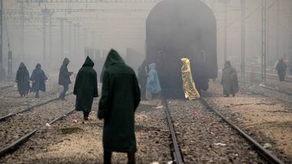 Refugiados caminan entre las vías del tren en Idomeni, Grecia