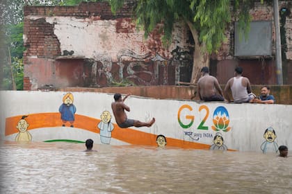 Residentes de las orillas del río Yamuna están sentados junto a una calle inundada en Nueva Delhi, India, jueves 13 de julio de 2023. Las inundaciones obligaron a evacuar a miles de personas en las zonas bajas de la capital.
