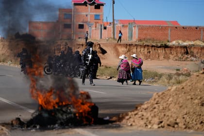 Residentes pasan junto a la policía cerca de barricadas levantadas por manifestantes antigubernamentales en una carretera en El Alto