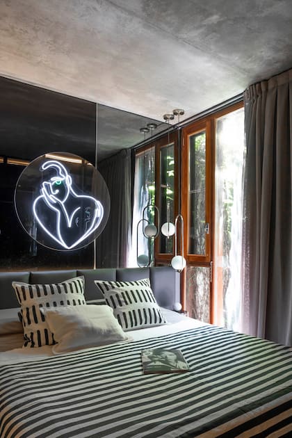 Respaldo de cama con canelones en cuero gris. Pared revestida con coverglass negro y espejo gris. En la cabecera, la obra de la diseñadora Julieta Otero en neón flex.