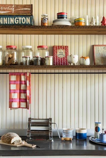 Revestimiento de madera dispuesta de forma vertical y estantes de pino Oregón con ménsulas recuperadas de una vieja cama de hierro. Mesada de cemento alisado, repasador (Franca Arts & Crafts) y contenedores de cerámica (Good Luck Casa).