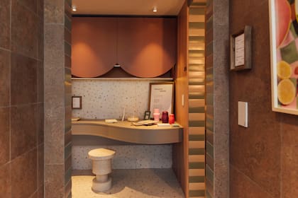 Rincón de trabajo de Jacinta, resuelto en el pasillo que va del estar al dormitorio, con escritorio curvo empotrado de melamina Gris Tapir (Faplac), banco "Ronda" (Par en Par), alacena en melamina Terracota (Faplac) y revestimiento de porcelanato Cesky Ivory (San Lorenzo Design) sobre la pared.