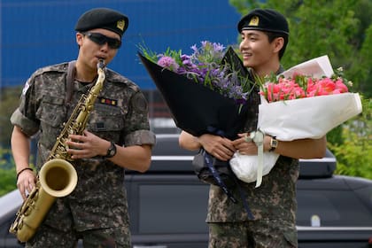 RM toca el saxo mientras V lo observa con dos ramos de flores en manos a la salida del centro deportivo al aire libre de Chuncheon, tras completar 18 meses de servicio militar
