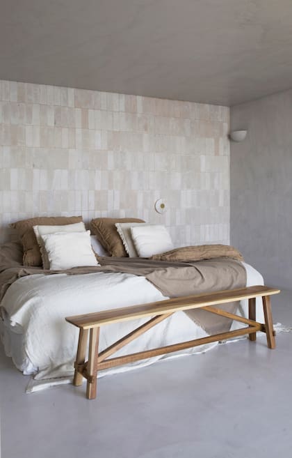 Ropa de cama (Casa Tarlo), pie de cama (Compañía Nativa), banco de madera recuperada (Estudio Trae). Apliques de alabastro (Dimm Iluminación). En la cabecera, revestimiento de ladrillos refractarios de cemento, que pone apenas un acento.