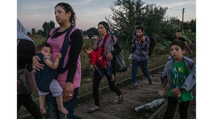 Roujin Sheikho, a la izquierda, de Siria, lleva a su hija y Widad Nabih, a la derecha, lleva a su hijo, caminan con otros refugiados sirios por las vias del ferrocarril antes de cruzar a Hungría desde Horgoš, Serbia
