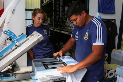 Rubén Gómez pega los números en las camisetas, Verónica observa.