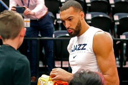 Rudy Gobert firma autógrafos después de los calentamientos, antes de un partido de la NBA contra Los Angeles Lakers en Salt Lake City, Utah. - El centro de Utah Jazz, Rudy Gobert, cuya prueba positiva de coronavirus provocó que la NBA cerrara su temporada, dice que el virus le ha hecho perder el sen