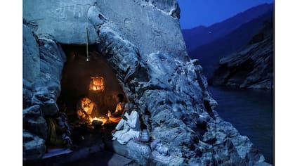 Sacerdotes hindúes se sientan dentro de una cueva mientras realizan oraciones vespertinas en las orillas del río Ganges en Devprayag