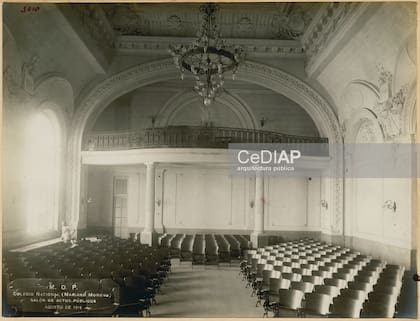 Salón de actos del Colegio Mariano Moreno, hacia 1915: filas de butacas, balcón superior, vitral y araña central componían el espacio que hoy es objeto de una restauración patrimonial integral