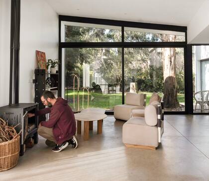 Santiago activa el fuego en el living ambientado con obras del estudio que fundó con Paz: sillón 'Cruce', la mesa baja 'Riel' y las lámparas de pie 'Acantilado', su última creación en luminarias.