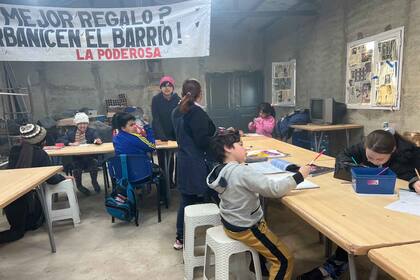 Santino y otros vecinos del barrio participan del apoyo escolar y de la merienda; el principal reclamo queda plasmado en el cartel: que urbanicen el barrio