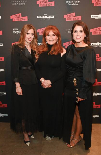 Sarah Ferguson, que combinó un vestido negro largo de noche con zapatillas glitter Gucci, posa rodeada por sus dos hijas: a la derecha, Eugenia, quien lució un diseño de satén de Peter Pilloto & Christopher de Vos adornado con un broche metálico dorado y sandalias Jimmy Choo; a la izquierda, Beatriz, con vestido midi de crêpe y chifón de la firma SelfPortrait y zapatos de gamuza con puntera de piel de serpiente, del diseñador Nicholas Kirkwood.