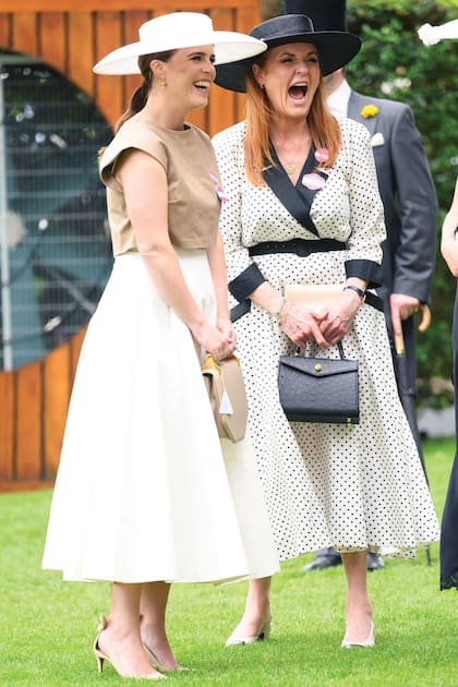 Sarah Ferguson y su hija, la princesa Eugenia, comparten un momento de diversión. Sarah, con un vestido vintage de Alistair Blair, cartera Ethan K, zapatos Chanel, sombrero de Jess Collett y brazalete de Van Cleef & Arpels de oro 18 quilates, y Eugenia con un look que ya usó en Trooping The Colour 2015 al que, en esta oportunidad, combinó con cartera de M2Malletier, zapatos Aquazurra, pamela de Emily London y pendientes de oro y diamantes de Sophie Lis.
