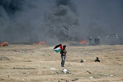 Un hombre sostiene una bandera palestina durante los enfrentamientos con las fuerzas israelíes cerca de la frontera entre la franja de Gaza e Israel