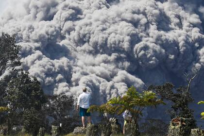 Un hombre tomas fotos a la gran columna que sale del volcán