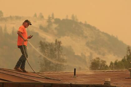 Un hombre moja los techos de su casa para evitar que se incendie