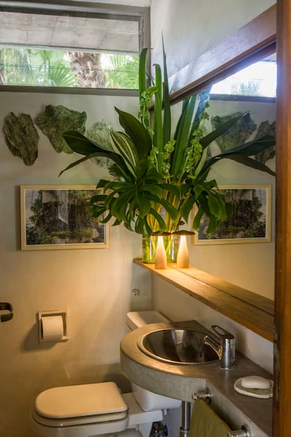 Se estiró la mesada en cemento alisado alrededor de la bacha para hacerla llegar en la pared y agregarle un toallero. La tabla de buena madera, más ancha en la base del espejo, brinda lugar de apoyo para objetos de tocador. O un lindo arreglo, como acá.