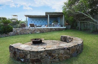 Se usó piedra del cerro para integrar con naturalidad el fogón y la galería, que a un costado esconde el lavadero y un depósito para bicicletas, reposeras y tablas de surf.