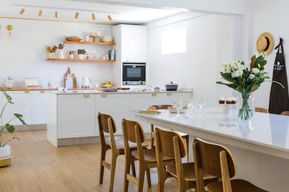 Muebles, mesada y estantes de madera (Lorien Mobile). Isla con tapa de Silestone ‘Blanco Norte’ (Mármoles De Stefano). Sillas (Unimate). Copas y cubiertos dorados (Philippa Deco Boutique). Platos de postre de cerámica artesanal (Candela González Arzac).Servilletas teñidas a mano y desflecadas (Timo