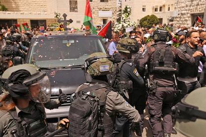 Las fuerzas de seguridad israelíes rodean un vehículo que transporta el féretro de la periodista asesinada de Al-Jazeera, Shireen Abu Akle, a la salida de un hospital, mientras los palestinos lanzan pétalos de rosa, antes de ser transportado a una iglesia y luego a su lugar de descanso, en Jerusalén, el 13 de mayo de 2022. 