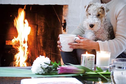 Hygge significa estar frente a la chimenea hogareña, leyendo un libro o mirando una buena serie, con muebles de madera y luces cálidas, junto a un ser querido, tomando una copa de vino, un café o una sopa rica