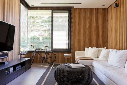 Sillón en L con funda de tussor crudo (Estudio LD/MB), persianas de madera (Riel Americano) y alfombra gris pizarra (Rug It). Para el centro se eligió un puf negro traído del exterior que sirve para sentarse y como mesa de apoyo.