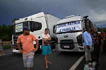 Simpatizantes del presidente Jair Bolsonaro se paran frente a camiones con mensajes relacionados con su lema de campaña, durante un bloqueo en la carretera Via Dutra BR-116 entre Río de Janeiro y Sao Paulo, en Barra Mansa en el estado brasileño de Río de Janeiro, el 31 de octubre de 2022.