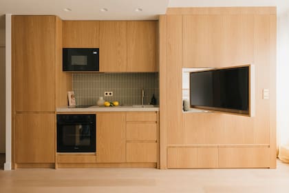 Sobre la derecha del mueble, los electrodomésticos panelables; horno y microondas en negro, igual que la pantalla de la tele. A los pies de esta, más cajones.