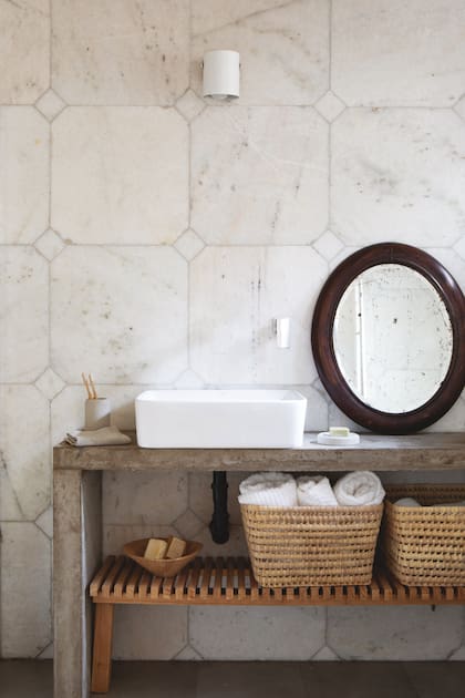 Sobre la mesada de cemento, bacha (Aqualia). El banco de madera con la medida justa organiza los canastos de fibras naturales (Zmarket), toallones (Luna Deco) y el bol de madera (Rajatabla) con jabones artesanales (Saponarium).