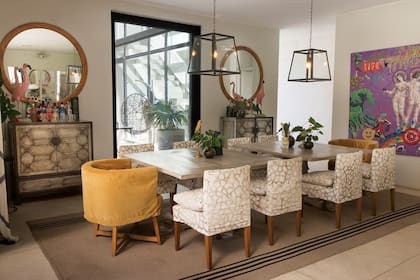 Sobre una de las paredes del comedor, a ambos lados del ventanal, hay dos espejos circulares y dos cómodas plateadas a la hoja. Las lámparas de techo son de hierro y vidrio. A las sillas con género
estampado, María le sumó dos sillones de terciopelo mostaza que custodian las mesas cuadradas, ubicadas en el centro. El cuadro es de Zelmira Peralta Ramos.