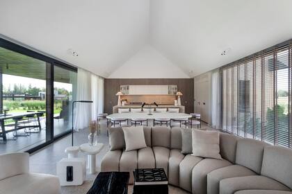 Sofá (Caro Bianco Interiors) acompañado por mesas de madera quemada (Concepto Calma). El hogar a gas tiene sobre él un módulo para la TV (El Corral Home).