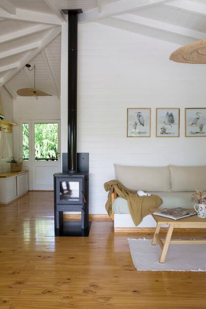 Sofá con almohadones a medida (Mora Lola) está pensado como un espacio para relajarse mirando de frente a la laguna. Salamandra (Fiamma) y lámpara colgante modelo ‘Palm Beach’ (El Almacén de Totó).