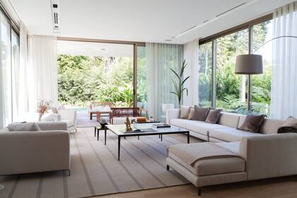 Sofá en L ‘Rey’; sillones tapizados en lino, mesas con estructura de hierro laqueado y tapas de vidrio y mármol (todo de XFB Arquitectura y Decoración). Lámpara de pie ‘Twiggy’ (Foscarini)