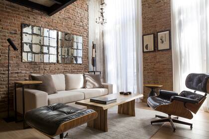 Sofá (Mar Deco), mesa ratona de petiribí macizo y mesa de apoyo en hierro y madera (Manifesto). Poltrona Eames Lounge, alfombra (Mihran) y espejo envejecido diseñado por la interiorista Silvina Piredda.