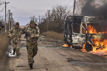 Soldados ucranianos pasan junto a un vehículo de voluntarios en llamas después de que un dron ruso lo golpeara cerca de Bakhmut, región de Donetsk, Ucrania, el jueves 23 de noviembre de 2023.