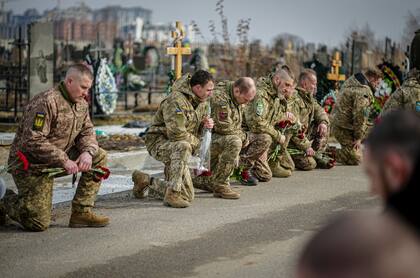 Soldados ucranianos se arrodillan al paso del féretro de un compañero en Bucha, uno de los escenarios de las mayores atrocidades rusas
