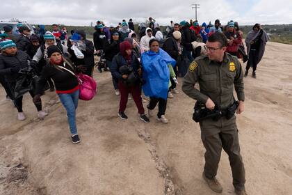 Solicitantes de asilo, incluidos algunos de Perú, caminan tras un agente de la Patrulla Fronteriza hacia una camioneta para ser procesados tras cruzar la frontera con México