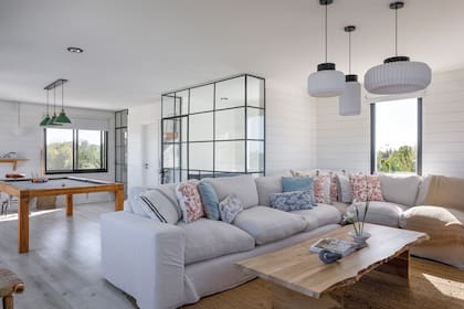 Steel frame (Ponasec) revestido con paneles de madera (Linke Maderas). Cerramiento de vidrio repartido y ventanales (AL13) con cortinas roller (Lux Roller). Piso ‘Rostock vinílico’ (Tucson). Sillón (Fradusco) con almohadones, mesa de centro y alfombra (todo de Ritta Estudio).
