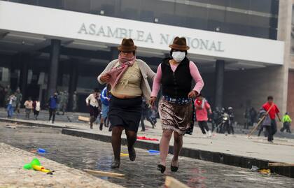 Dos mujeres corren para evitar el enfrentamiento frente a la Asamblea Nacional