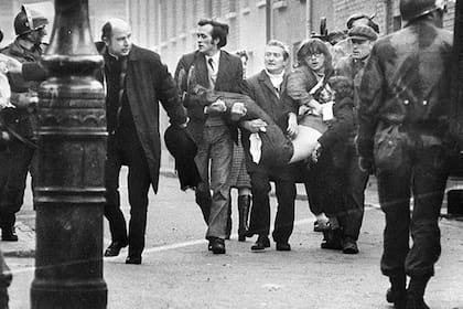 El cuerpo de Jackie llevado hacia afuera de la balacera; el padre Daily, a la izquierda de la imagen, llevaba un pañuelo blanco en la mano para abrirse paso entre la gente y los paracaidistas británicos