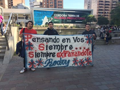 Sus amigos llevan una bandera con la frase "Pensando en vos siempre, siempre extrañandote" a cada lado que van