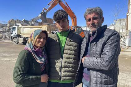 Taha Erdem, de 17 años, en el centro, su madre Zeliha Erdem, a la izquierda, y su padre Ali Erdem posan para una fotografía junto al edificio destruido donde Tahan quedó atrapado tras el terremoto del 6 de febrero, en Adiyaman, Turquía, el viernes 17 de febrero de 2023. Taha Erdem, residente de Adiyaman, en el sureste de Turquía, es uno de los cientos de supervivientes sacados de edificios derrumbados tras el fuerte terremoto del 6 de febrero. Erdem, de 17 años, se grabó a sí mismo con su teléfono mientras estaba atascado y atrapado entre el hormigón en lo que pensó que serían sus últimas palabras. (AP Photo/Mehmet Mucahit Ceylan)