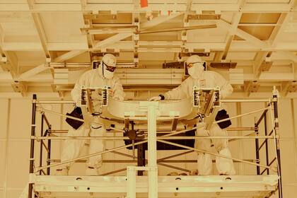 Técnico utilizando el microscopio para inspeccionar la oblea de silicio con chips de ordenador en la sala limpia de producción