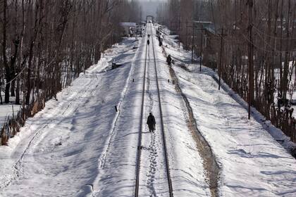 Varias personas caminan por la vías del tren que fue cancelado por las intensas nevadas en Srinagar, India