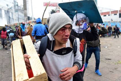 Un manifestante herido en el rostro utiliza un cajón como escudo