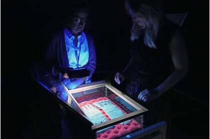 Tessa Gadomski (izquierda), bibliotecaria de conservación, y Alicia Meyer (derecha), curadora de servicios de investigación de las Bibliotecas, examinando los legendarios guantes con luz ultravioleta