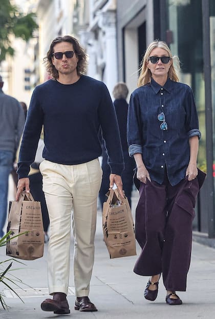 Todo un caballero. Mientras Falchuk carga las bolsas, la actriz advierte la presencia de los paparazzi con un gesto de asombro. Para ir de compras, Paltrow combinó una camisa de jean oscuro con pantalones cargo y guillerminas al tono