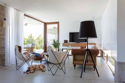 Toda la planta baja tiene piso de porcelanato ‘Garage Toffee’ (SBG). Sillón Chesterfield (Erzebet Restoration) con almohadones y manta (Gloria Atelier Deco). Sillas BKF (Pasto Home Shop) y lámpara de tres patas (La Pantalla).